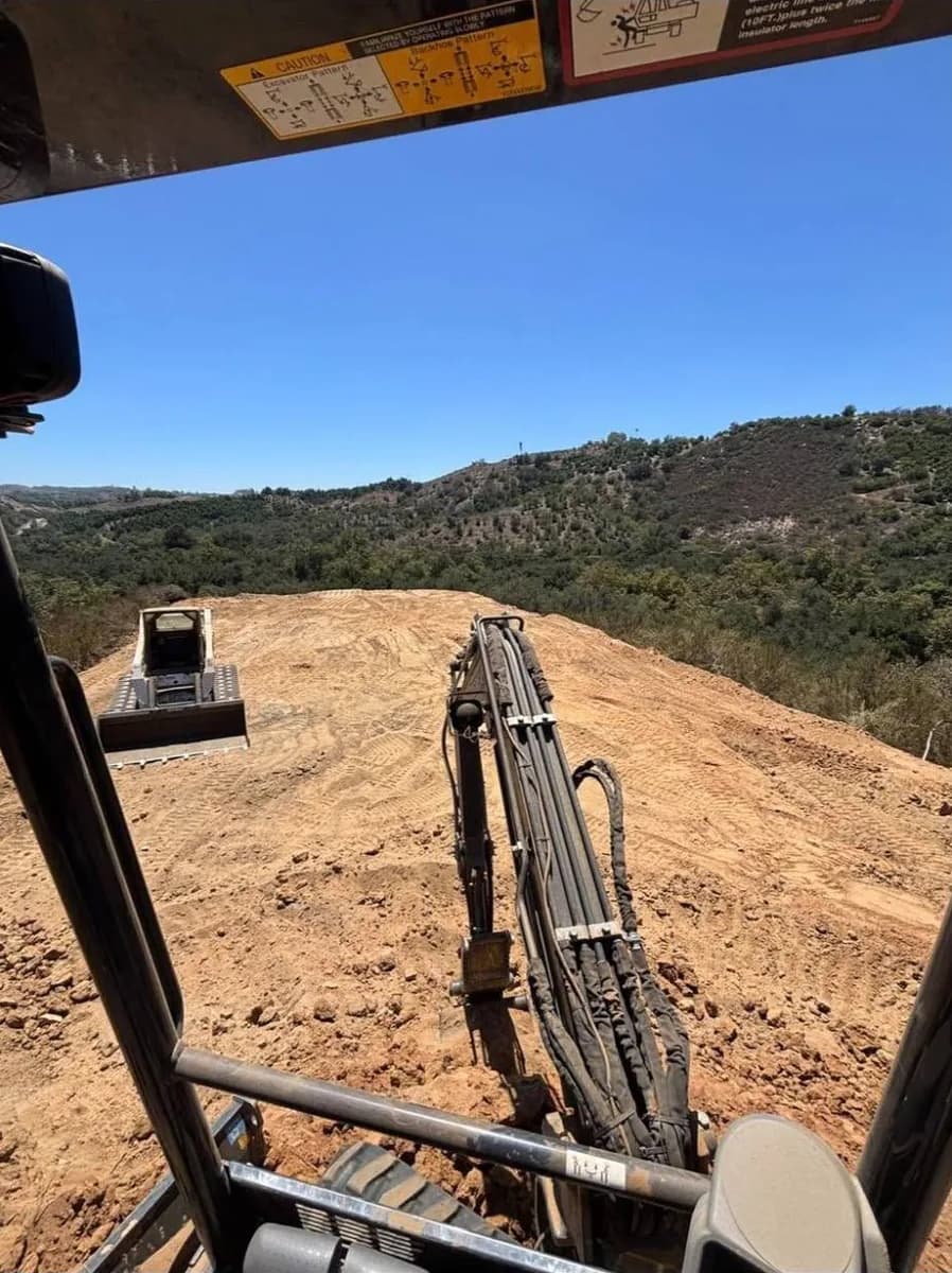 Freshly graded hilltop pad in Fallbrook with the Bobcat T300 and avocado groves behind